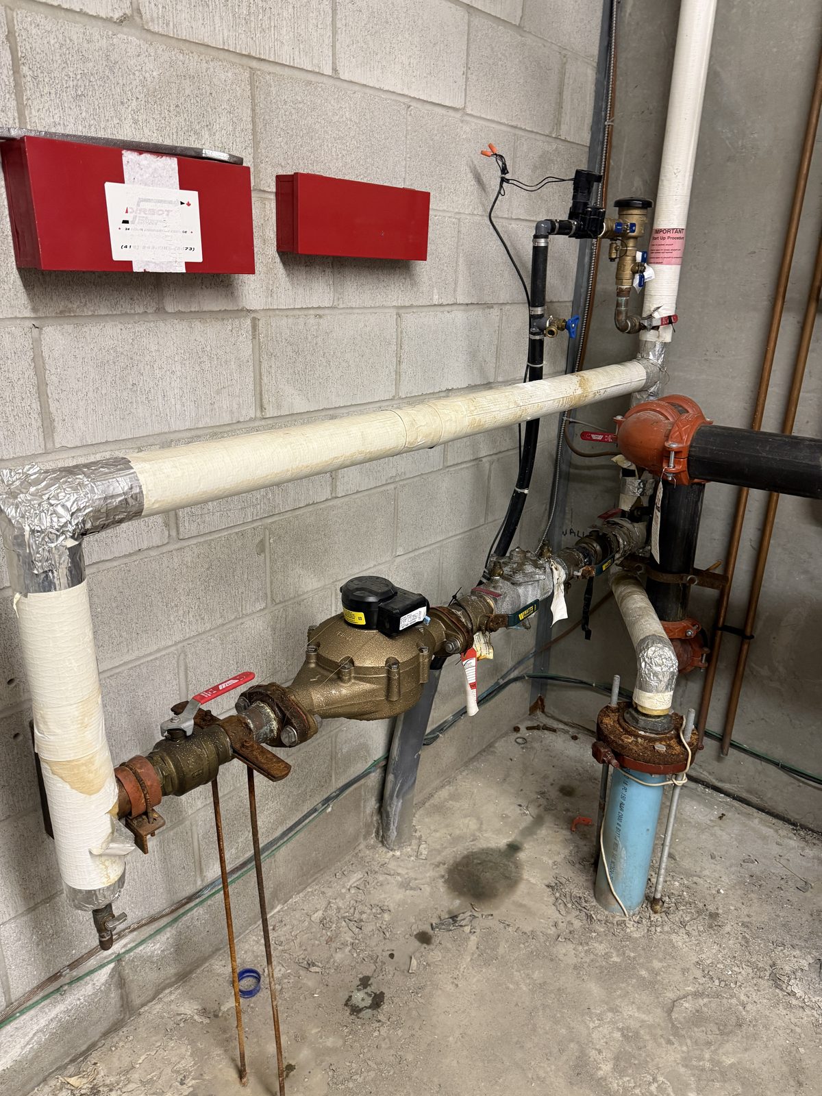 The old water service entry: insulated pipe, meter and valves beside a fire sprinkler riser