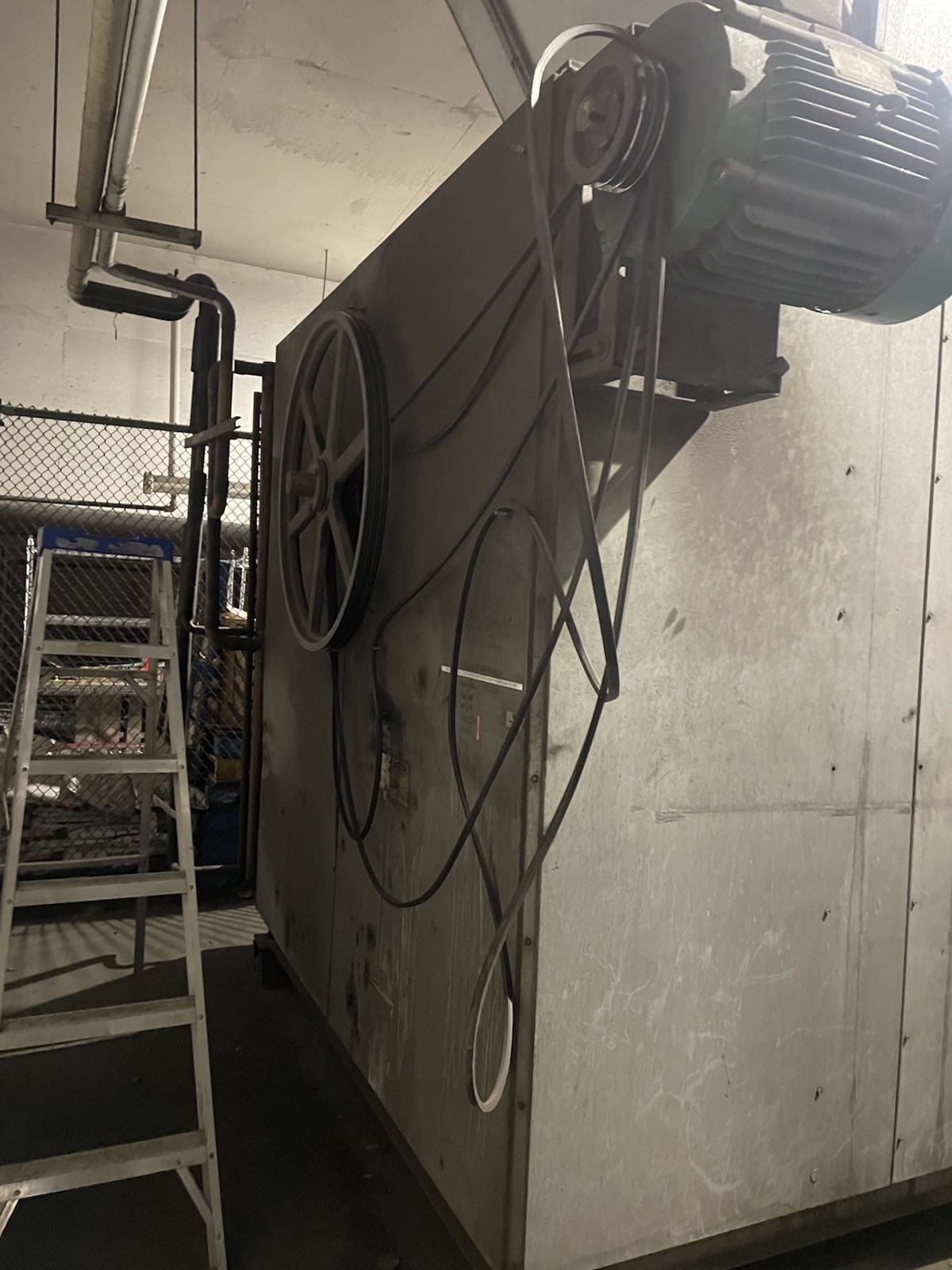 A large grey air-handling unit with its belt drive exposed: the fan pulley on the cabinet, the 30 HP motor mounted above, and the old belts hanging off the drive