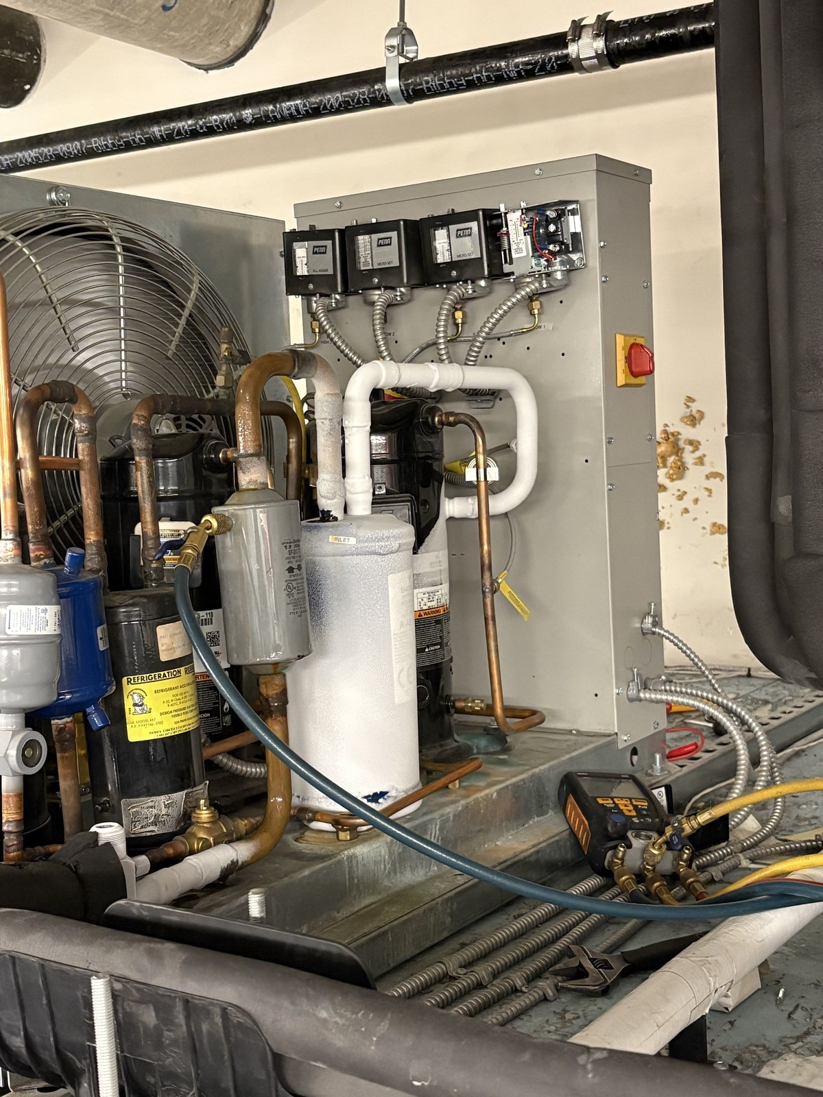 A condensing unit with frost on the suction accumulator, pressure controls on the open panel and refrigeration gauges connected on the base