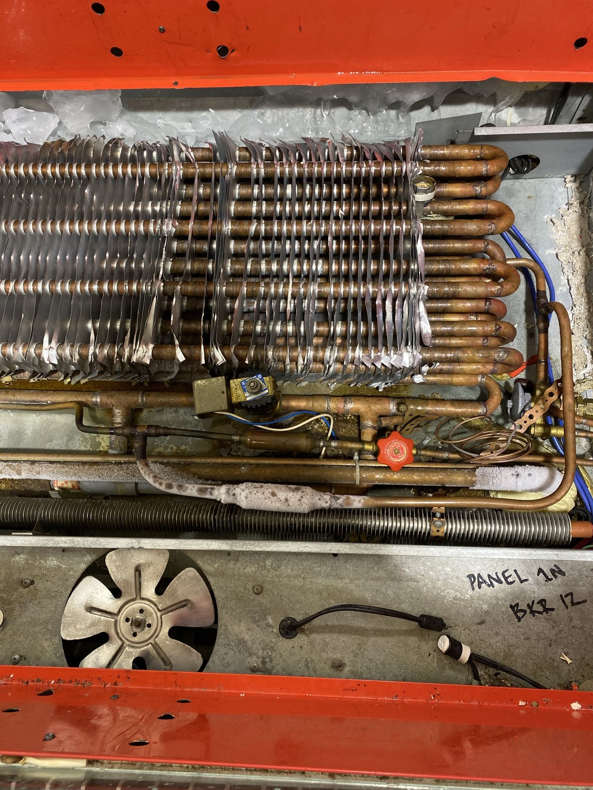 An evaporator coil inside a red-framed refrigeration unit, iced over along the top with bent fins, the expansion valve, a solenoid valve and the fan below