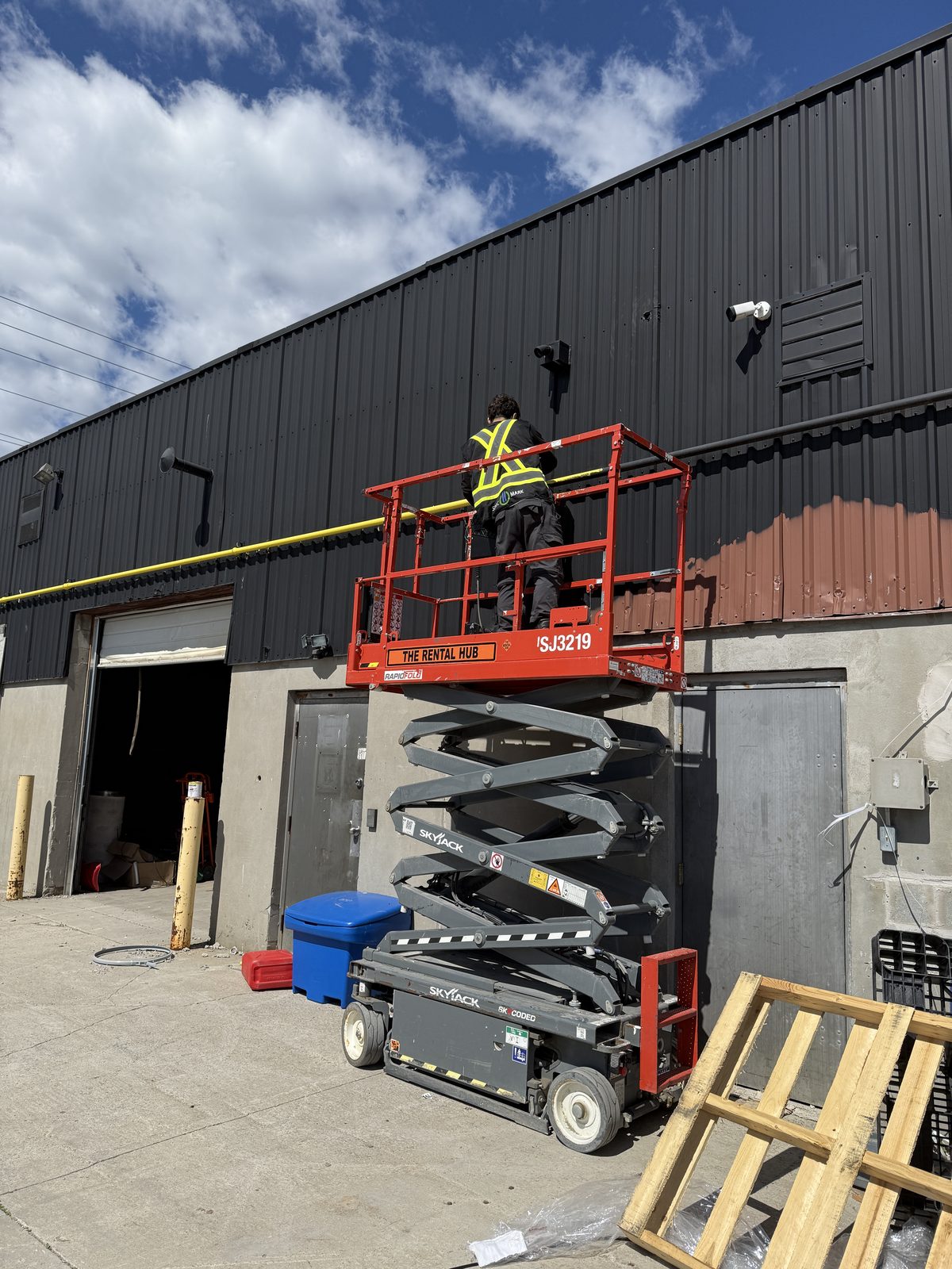 Technician on a lift securing a yellow-painted gas line to a steel building