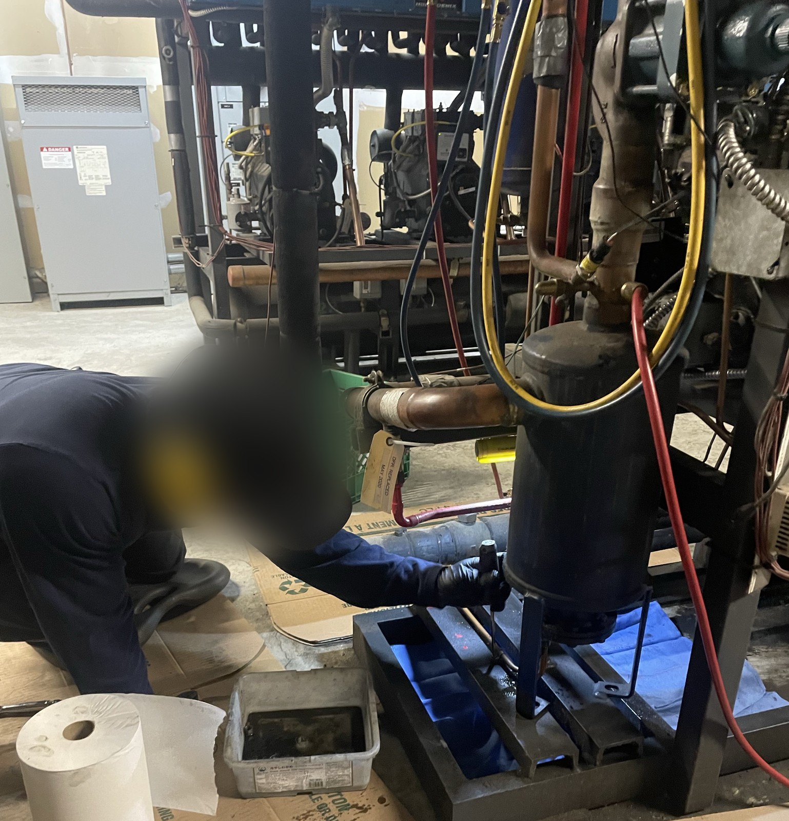 Technician kneeling at the base of the compressor rack with a drain pan, during preventative maintenance