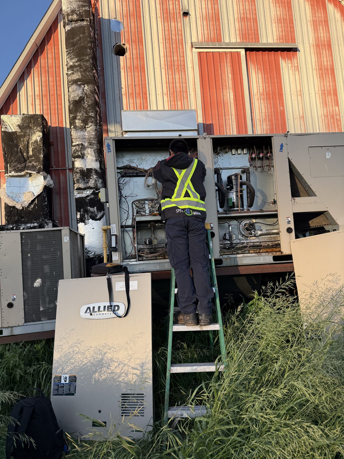 Technician on a ladder working inside an open rooftop unit