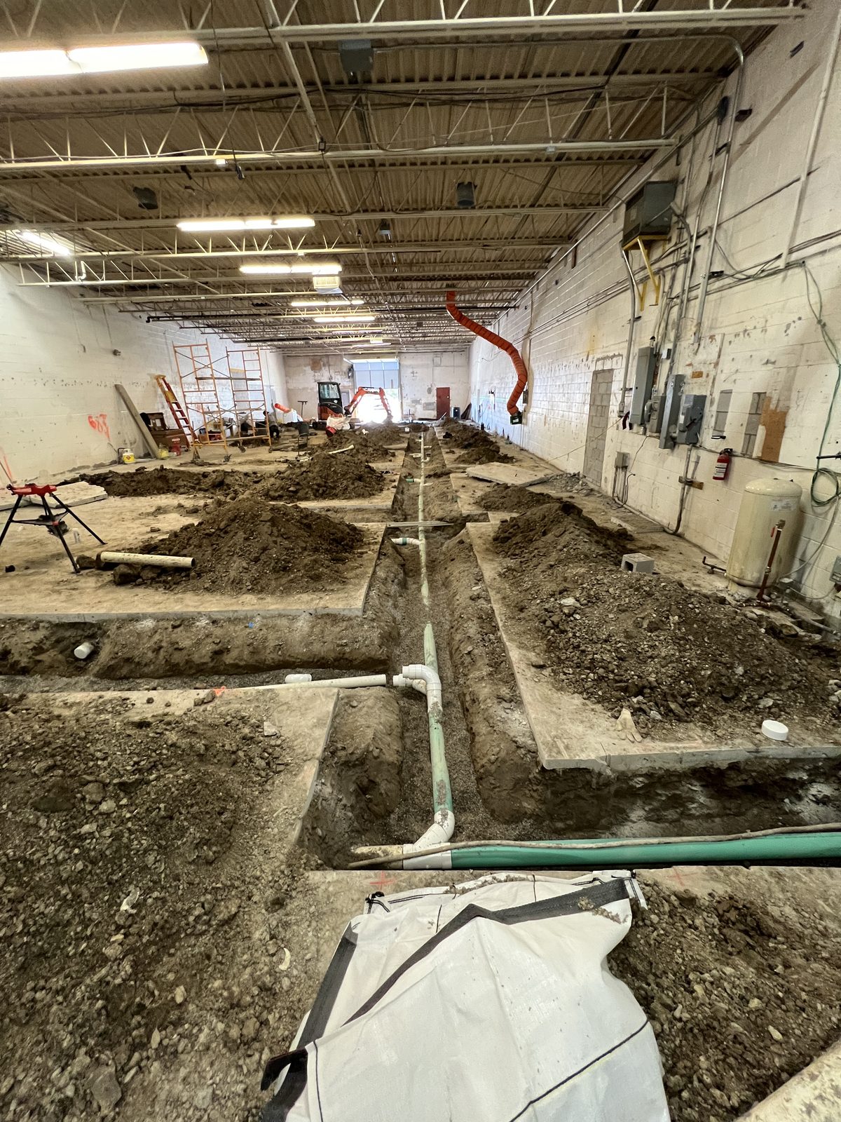 Green PVC drainage pipe laid in the trench, running the length of the unit