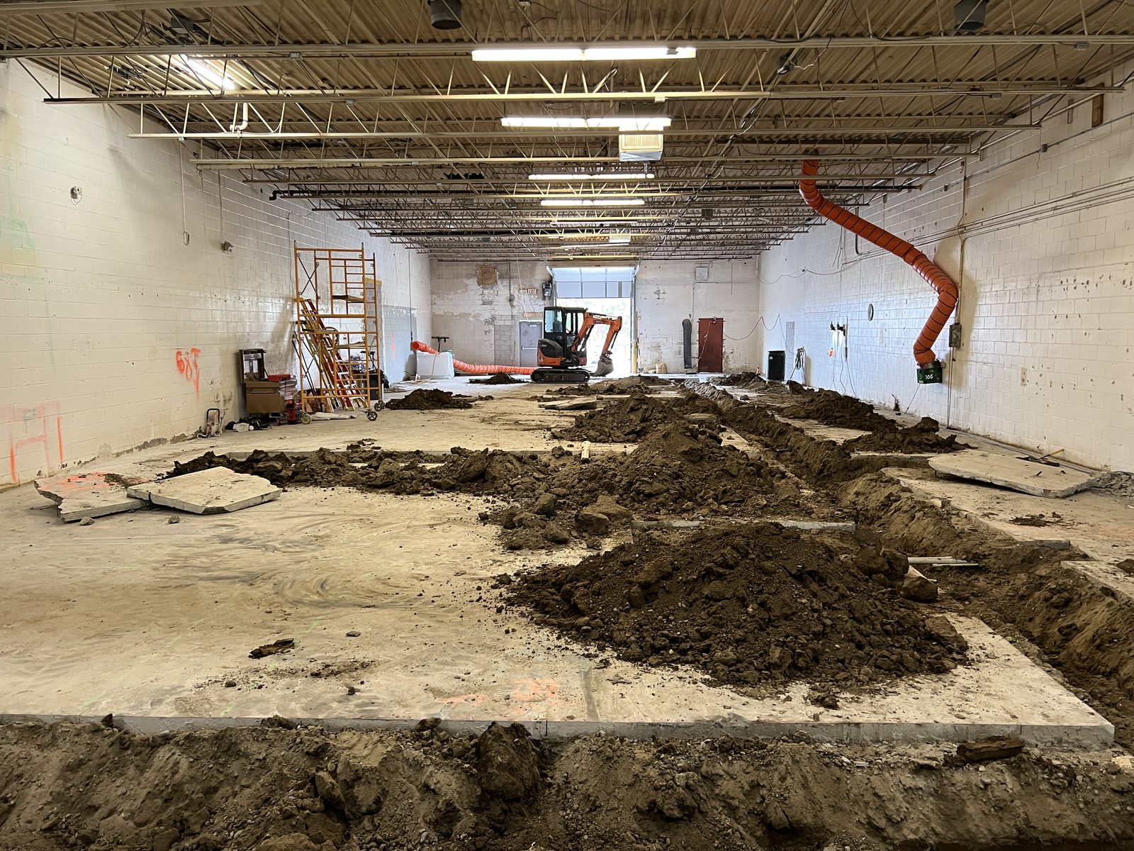 Open trenches across the warehouse floor with a mini excavator at the far end
