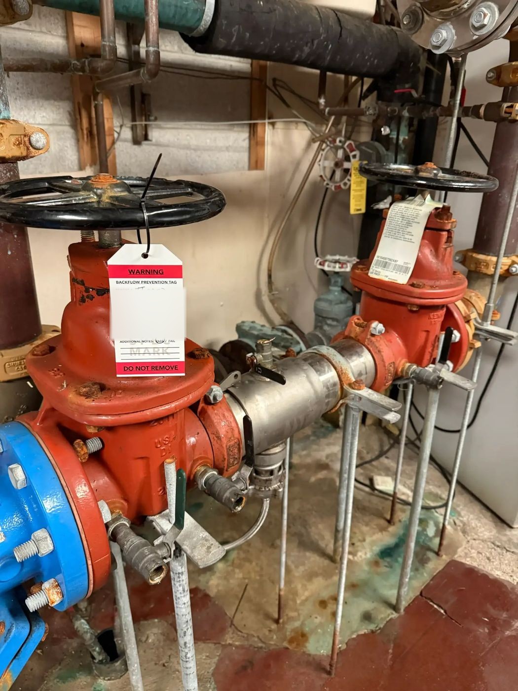 Red 4-inch RPZ backflow assembly with a Spec-Mark test tag attached, in a mechanical room