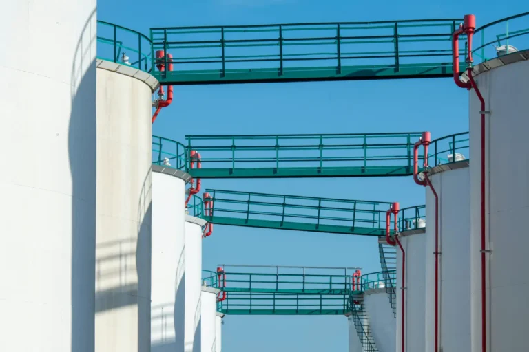 Large white industrial water storage tanks connected by green walkways and red pipes under blue sky.