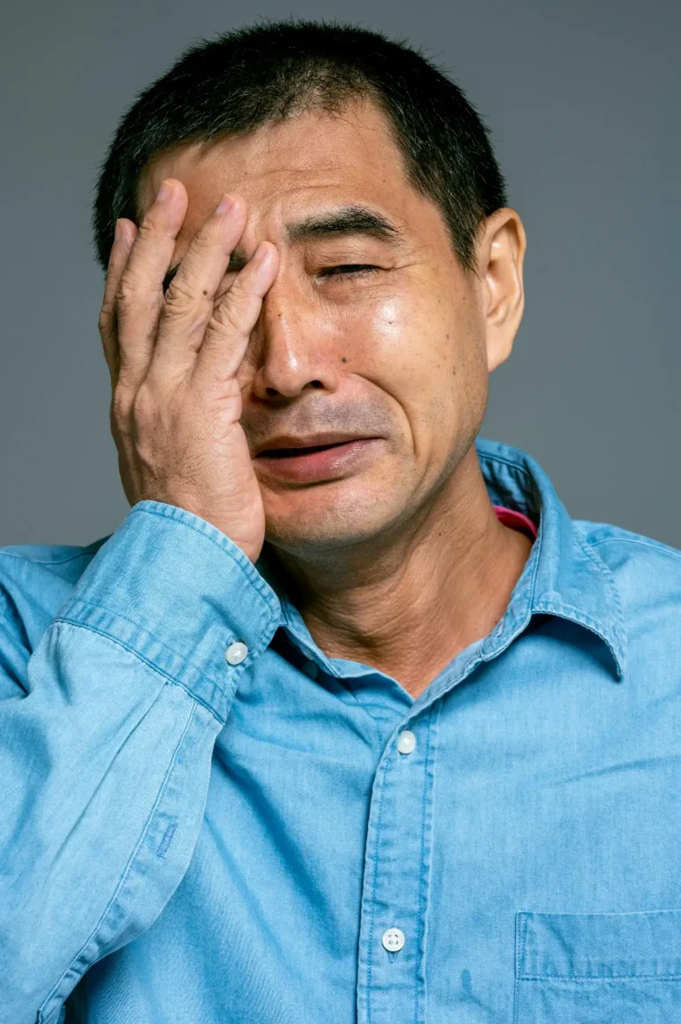Middle-aged man in a blue cotton shirt covering his face with his hand, looking stressed.