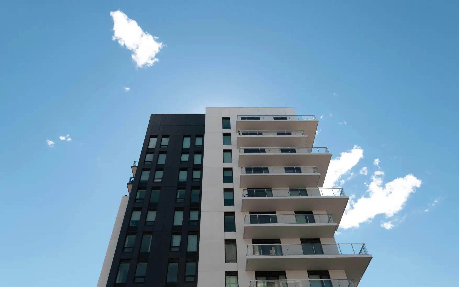 Modern apartment building with glass balconies and contrasting white and dark facade against a clear blue sky